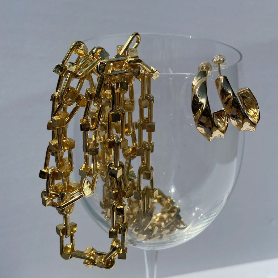gold u link chain necklace and a pair of gold hoop earrings hanging from a wine glass
