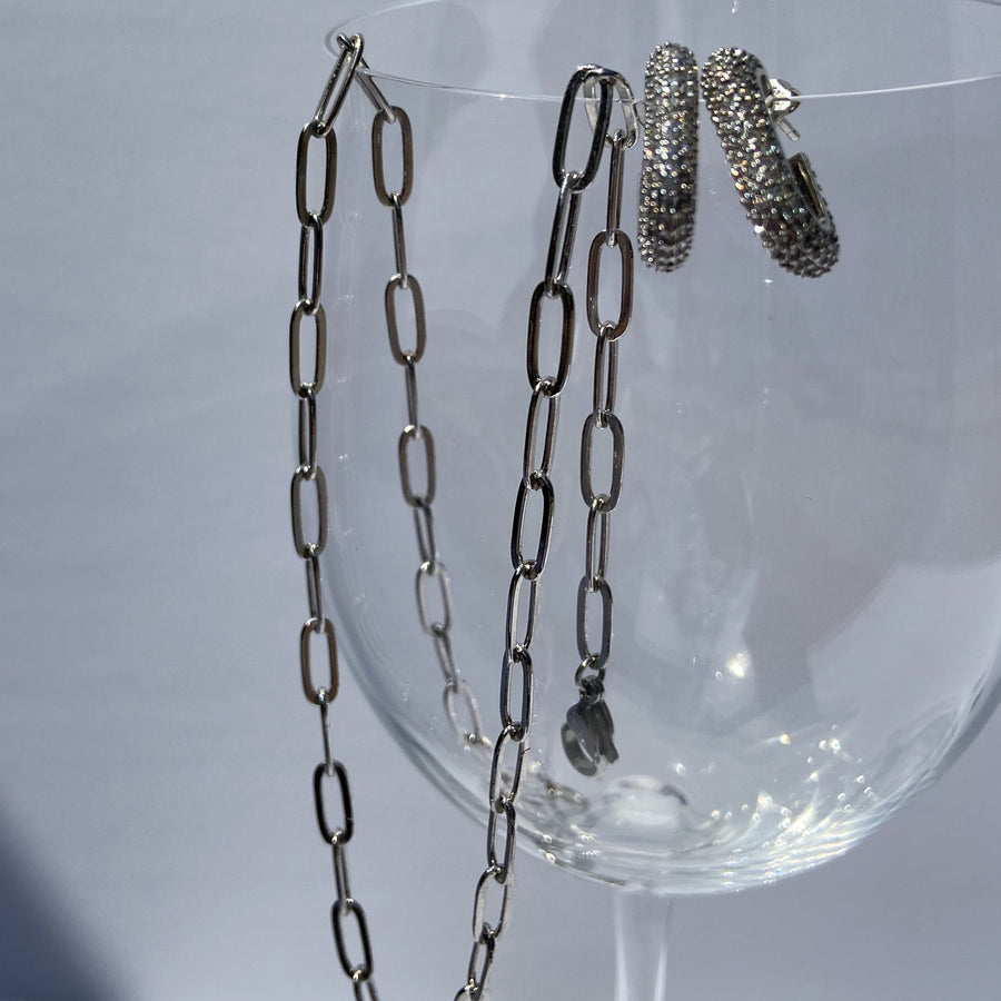 white gold paperclip chain necklace and a pair of white gold earrings hanging from a wine glass